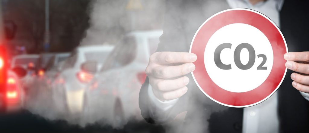Panneau d'interdiction portant la mention CO2 tenu devant une file de voitures dans un nuage de gaz d'échappement